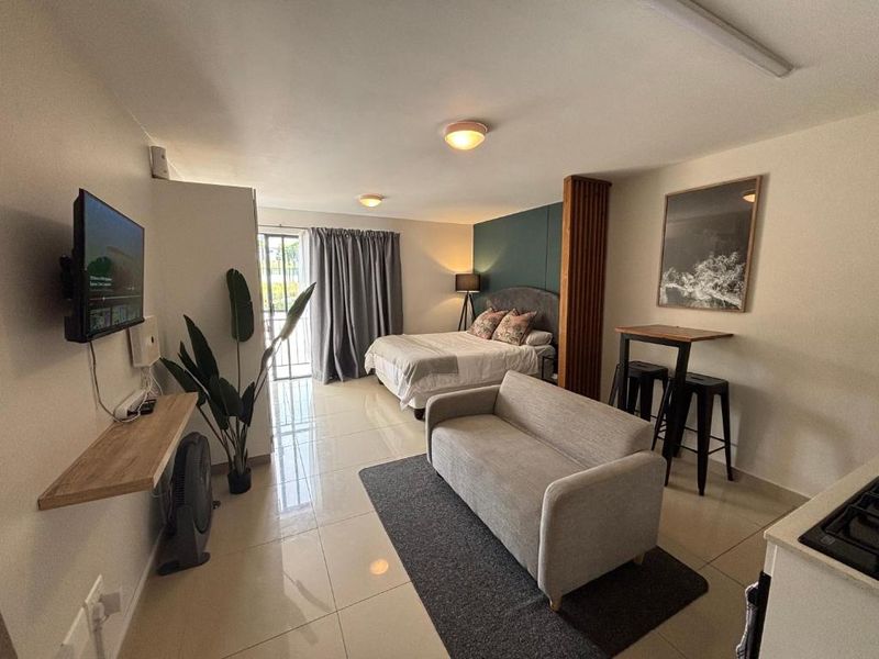 A well-maintained open-plan studio apartment featuring tiled flooring, a functional room divider, and direct access to a balcony through a sliding glass door.