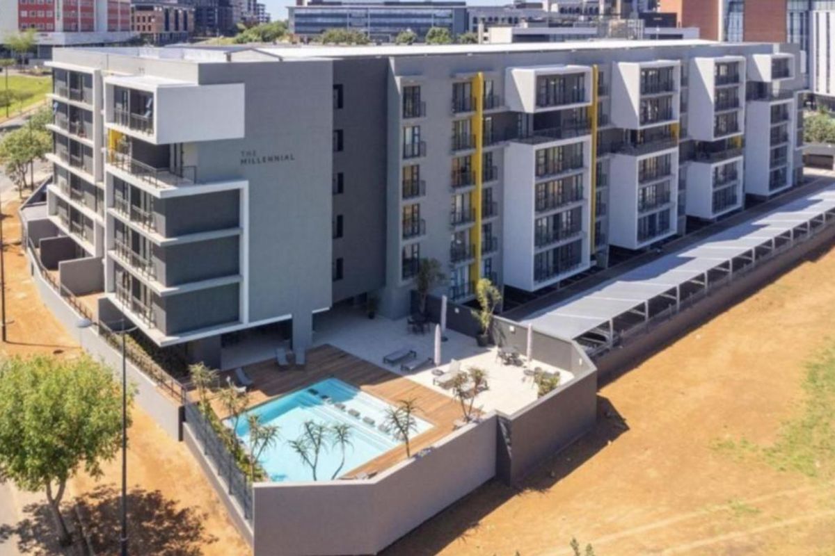 Aerial view of a modern apartment complex featuring a swimming pool, wooden deck, and covered parking facilities.
