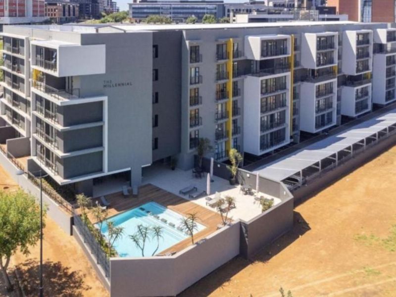 Aerial view of a modern apartment complex featuring a swimming pool, wooden deck, and covered parking facilities.