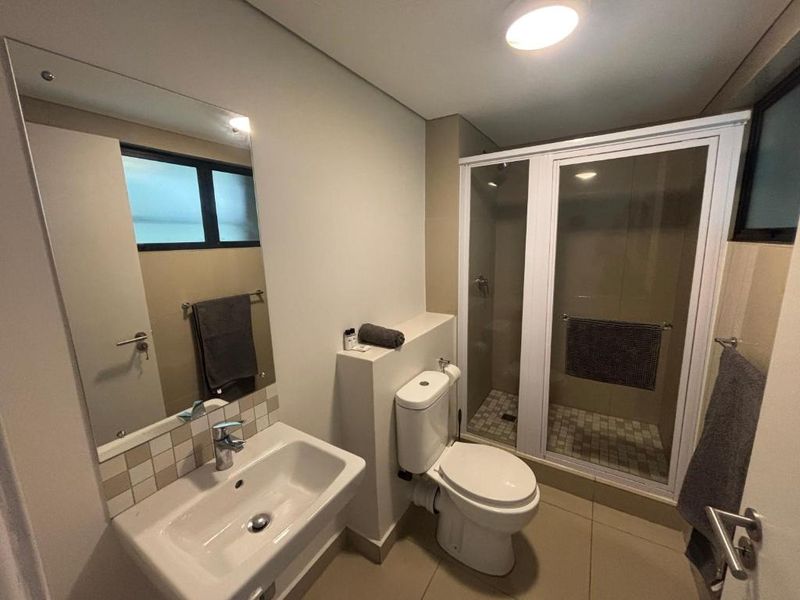A clean and functional bathroom featuring a wall-mounted basin, a toilet, and a separate shower enclosure with tiled finishes.