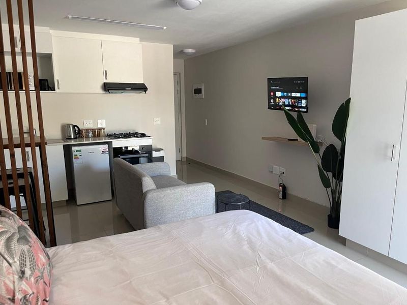 Compact open-plan studio apartment featuring a kitchenette with built-in cabinetry, gas hob, and oven, alongside a functional living and sleeping area with tiled floors.