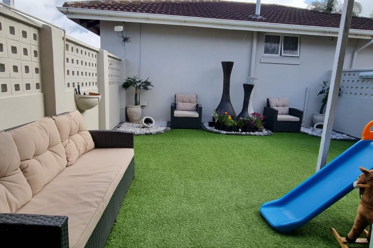 A well-maintained rear courtyard featuring artificial turf, decorative breeze block boundary walls, and a tiled roof structure.