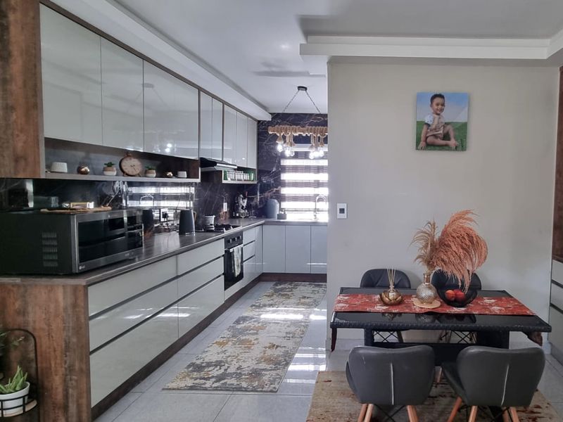 Modern open-plan kitchen and dining area featuring sleek high-gloss cabinetry, integrated appliances, and contemporary finishes throughout.