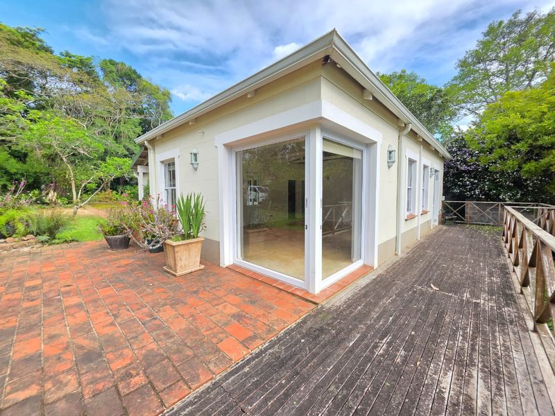 Rear exterior view of the cottage featuring a terracotta patio, timber decking with balustrade, and modern corner sliding glass doors.