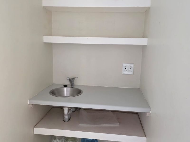 A compact utility or scullery area featuring a small stainless steel sink, built-in shelving, and a functional countertop.
