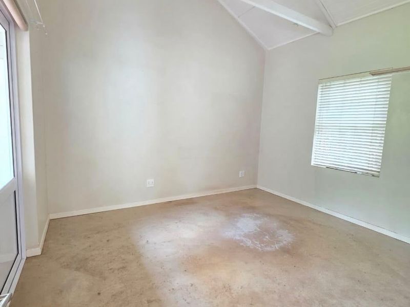 An empty bedroom featuring a high vaulted ceiling with exposed rafters, a ceiling fan, and a sliding glass door leading outdoors.