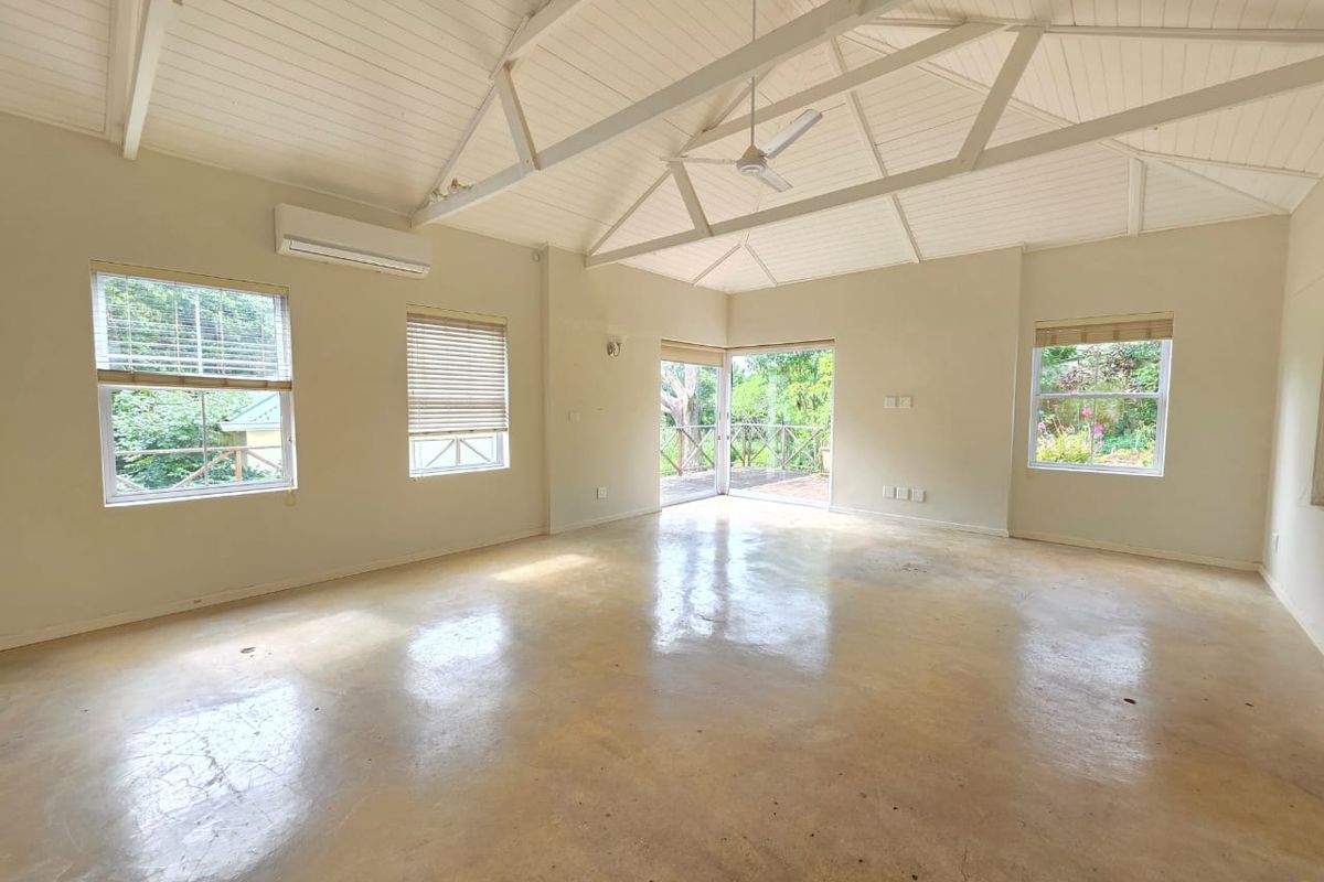 Spacious living area featuring a vaulted timber ceiling with exposed trusses, polished concrete floors, split-system air conditioning, and direct access to an outdoor deck.
