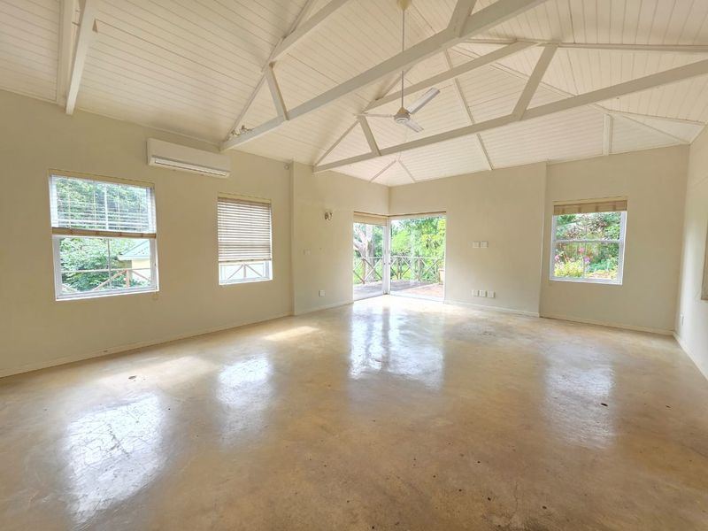 Spacious living area featuring a vaulted timber ceiling with exposed trusses, polished concrete floors, split-system air conditioning, and direct access to an outdoor deck.
