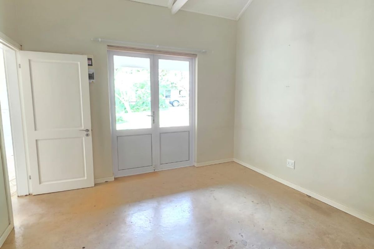 A bright, empty bedroom featuring a high vaulted ceiling with exposed rafters, a ceiling fan, and french doors leading to the exterior.