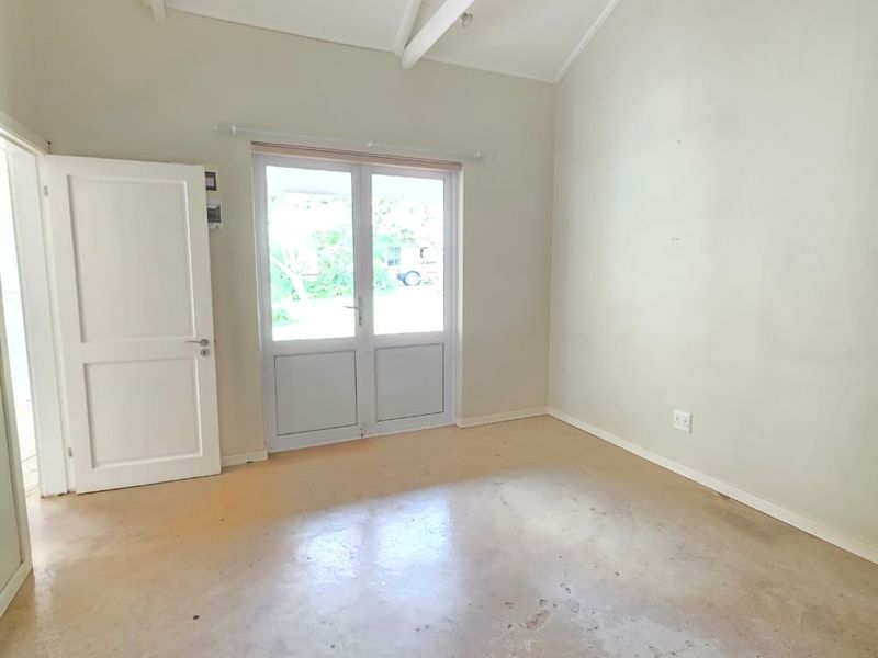 A bright, empty bedroom featuring a high vaulted ceiling with exposed rafters, a ceiling fan, and french doors leading to the exterior.