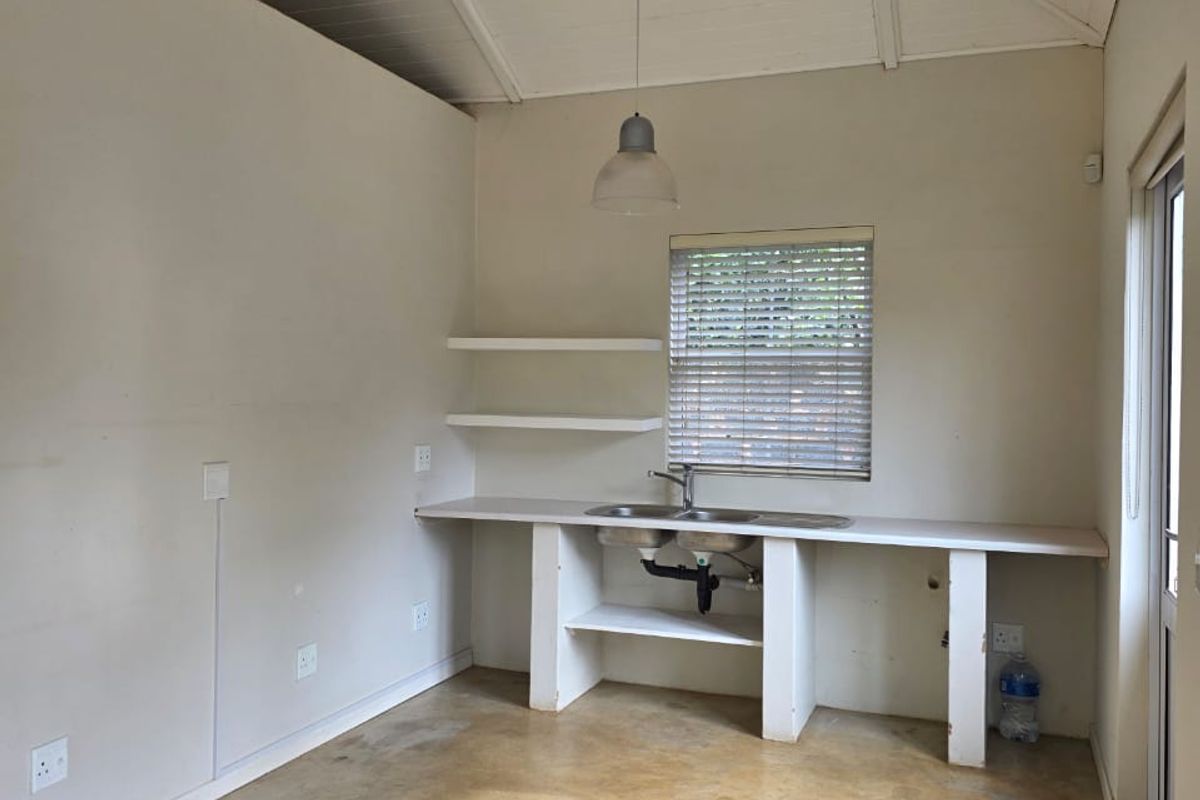A compact, empty kitchen area featuring a vaulted ceiling, exposed rafters, concrete flooring, and a basic built-in sink unit with open shelving.