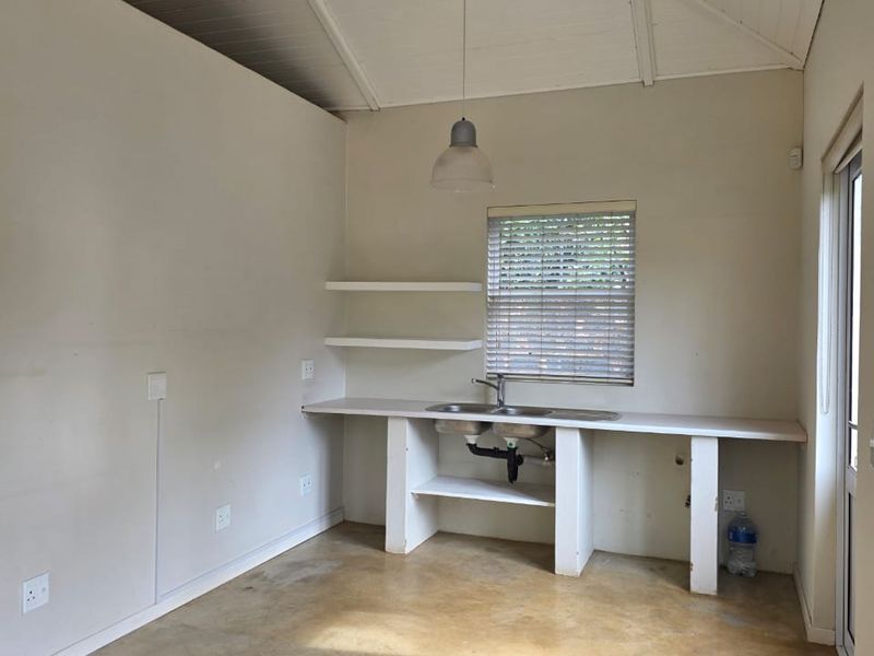 A compact, empty kitchen area featuring a vaulted ceiling, exposed rafters, concrete flooring, and a basic built-in sink unit with open shelving.