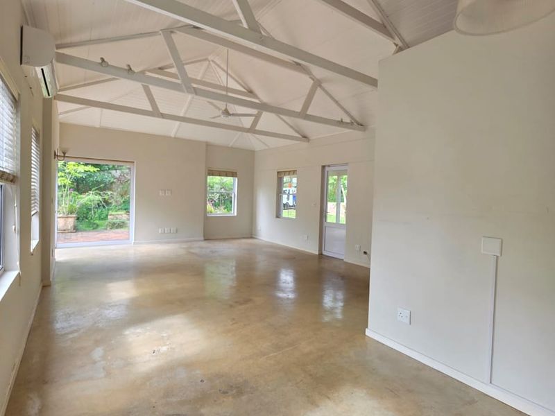 Spacious open-plan living area featuring high exposed truss ceilings, polished concrete floors, and direct access to the garden through sliding glass doors.