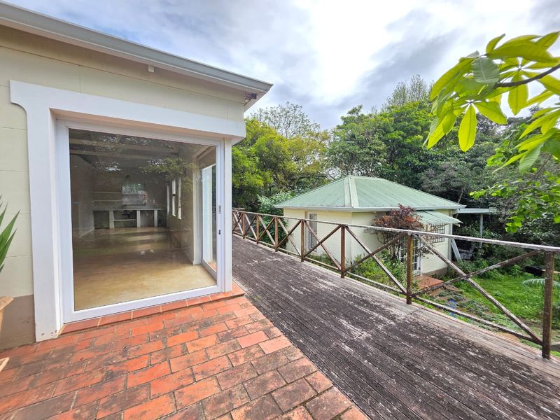 Elevated timber deck with terracotta tiled section and wooden balustrade, offering an outdoor transition space overlooking the garden and secondary cottage structure.