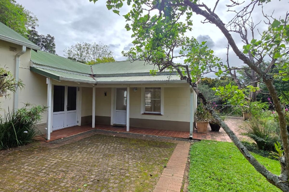 Rear view of the cottage featuring a covered veranda, brick paved patio area, and established garden surroundings.