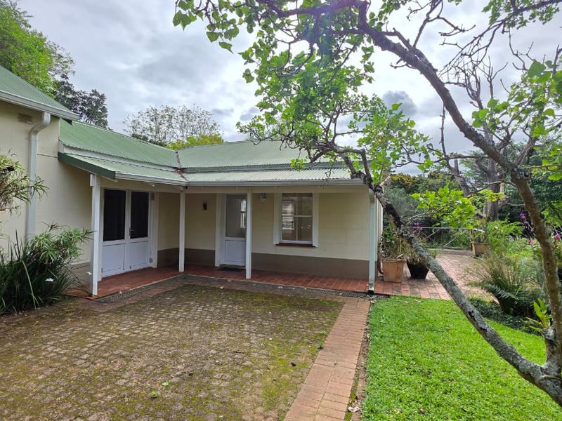 Rear view of the cottage featuring a covered veranda, brick paved patio area, and established garden surroundings.