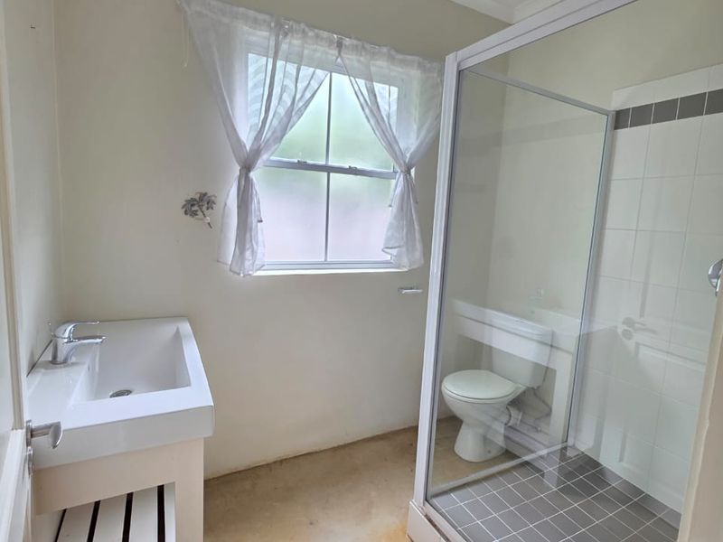 A functional bathroom featuring a vanity basin, a glass-enclosed shower, and a toilet, with neutral wall finishes and concrete flooring.
