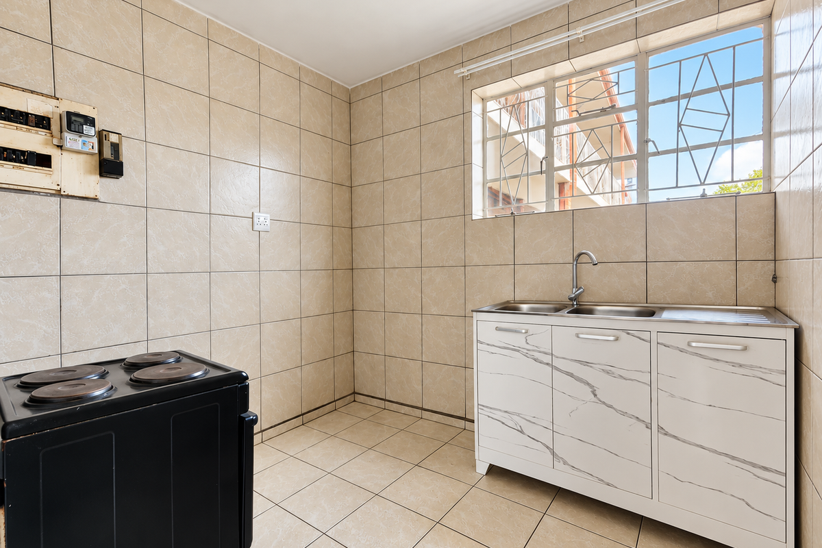 A functional kitchen area featuring fully tiled walls and floors, a stainless steel sink unit with a mixer tap, and a window with security bars.
