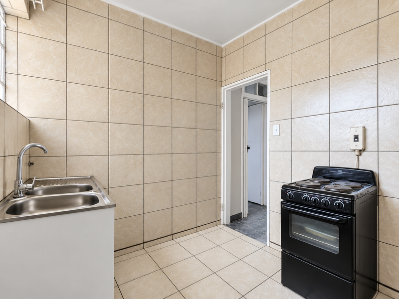 A functional kitchen area featuring full-height ceramic wall tiling, tiled flooring, a double bowl stainless steel sink, and a freestanding electric stove.