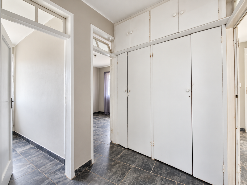 A bright hallway featuring extensive built-in cupboards with overhead storage, dark tiled flooring, and transom windows allowing natural light flow between rooms.