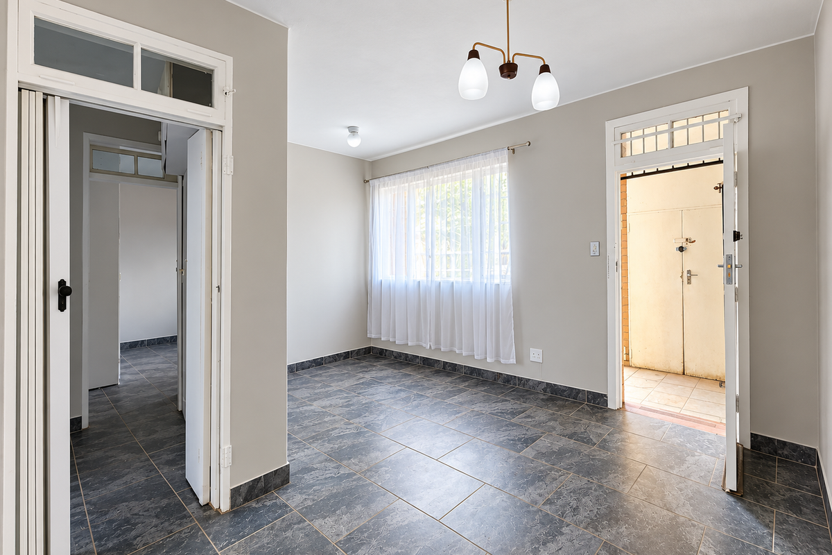 A bright, empty living area featuring neutral walls, dark tiled flooring, and direct access to both an internal hallway and an external entrance.