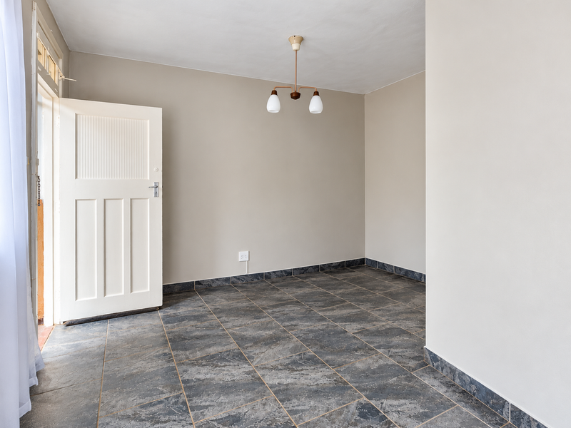 A bright, empty living area featuring neutral walls, dark tiled flooring, and a classic pendant light fixture with direct access to an outdoor space.