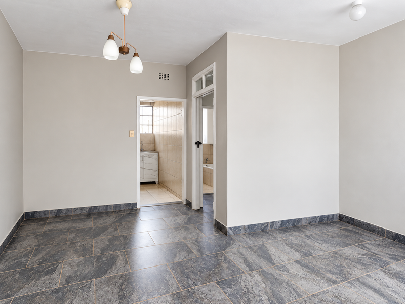 A bright, empty living area featuring neutral walls and modern grey tiled flooring, providing a clean and versatile space for interior design.