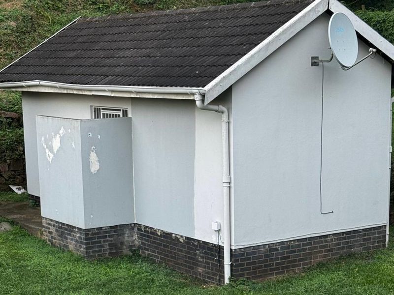 Rear view of a cottage featuring a tiled roof, brick plinth, and exterior wall with a satellite dish.