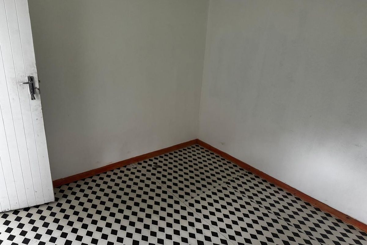 An empty bedroom featuring classic black and white checkered vinyl flooring and timber skirting boards, ready for a fresh coat of paint.