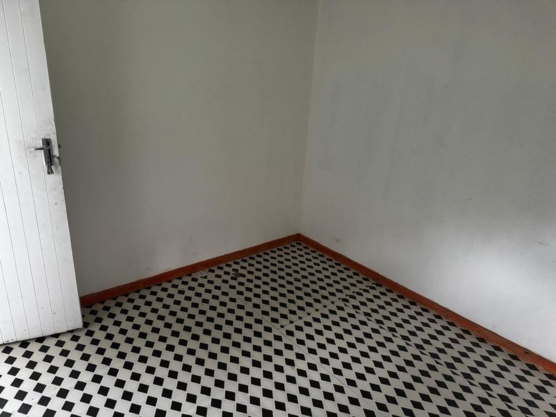 An empty bedroom featuring classic black and white checkered vinyl flooring and timber skirting boards, ready for a fresh coat of paint.