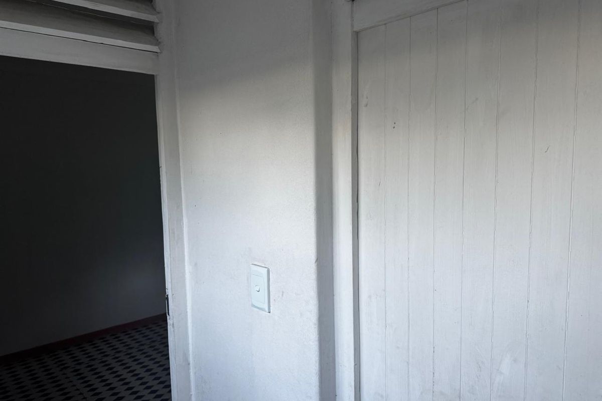 A simple hallway area featuring a built-in cupboard, louvre window, and patterned tiled flooring, showing signs of wear and requiring cosmetic updates.