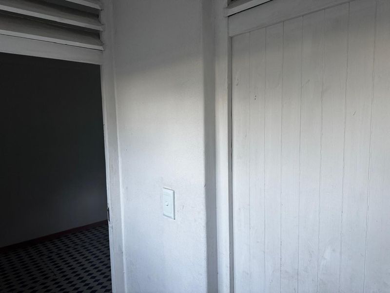 A simple hallway area featuring a built-in cupboard, louvre window, and patterned tiled flooring, showing signs of wear and requiring cosmetic updates.