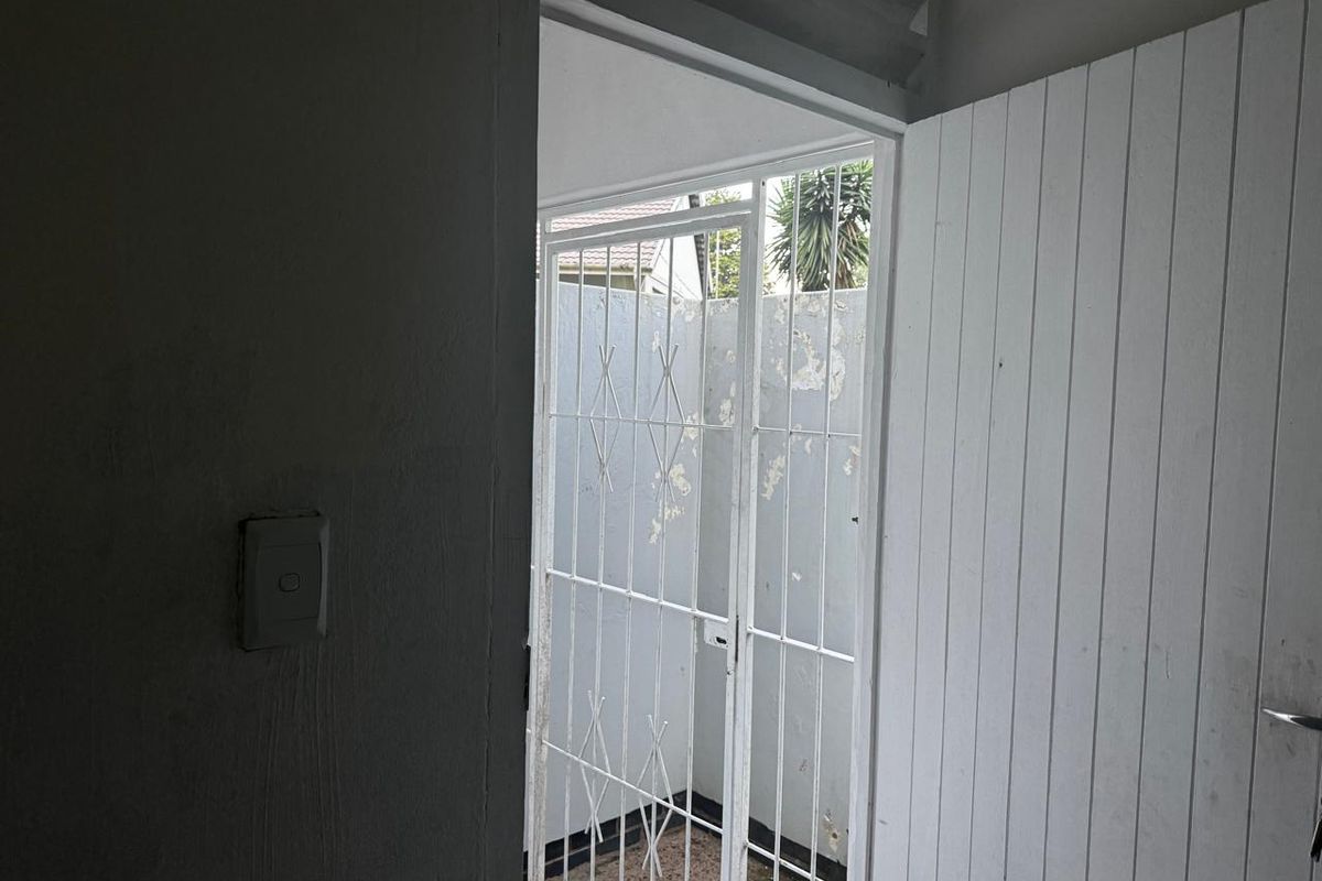 An interior view of an entryway featuring a white timber door and a metal security gate leading to an exterior area.