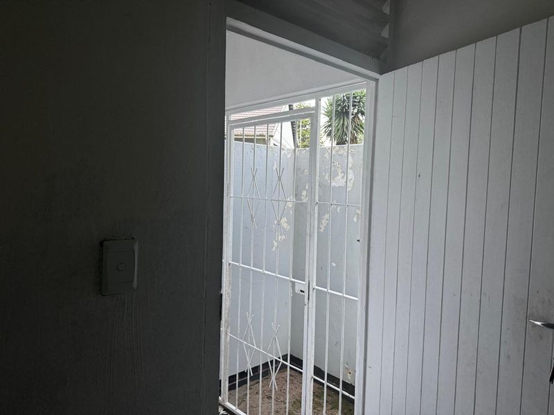 An interior view of an entryway featuring a white timber door and a metal security gate leading to an exterior area.