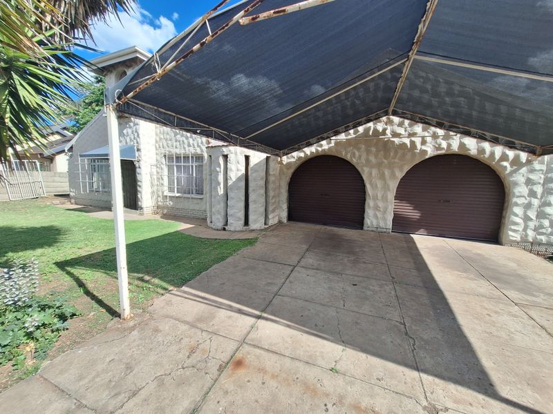 Front exterior view featuring a double garage with stone-clad facade, a shade cloth carport, and a concrete driveway.