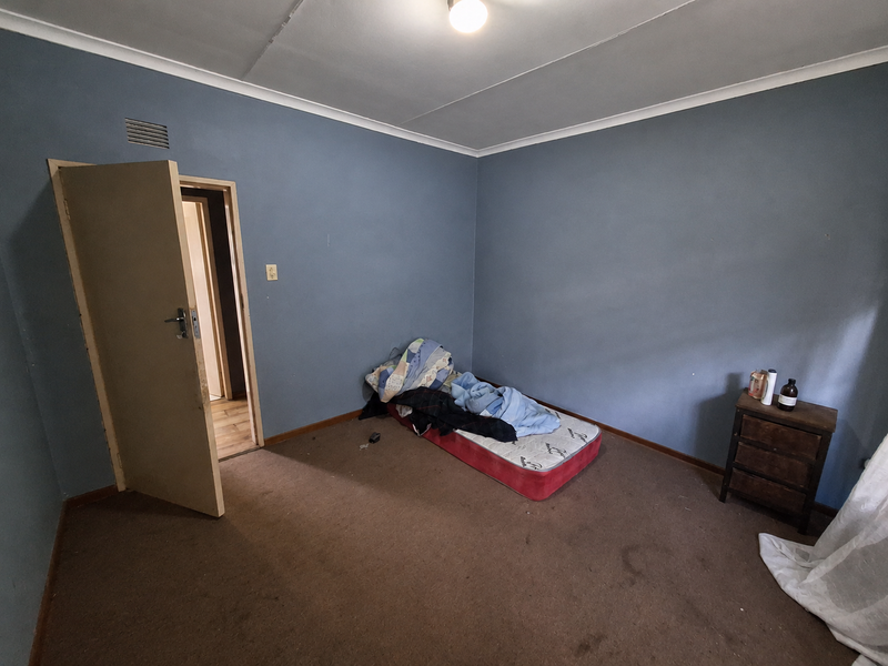 A sparsely furnished bedroom featuring blue walls, carpeted flooring, and a ceiling ventilation grille, offering a blank canvas for potential renovation.