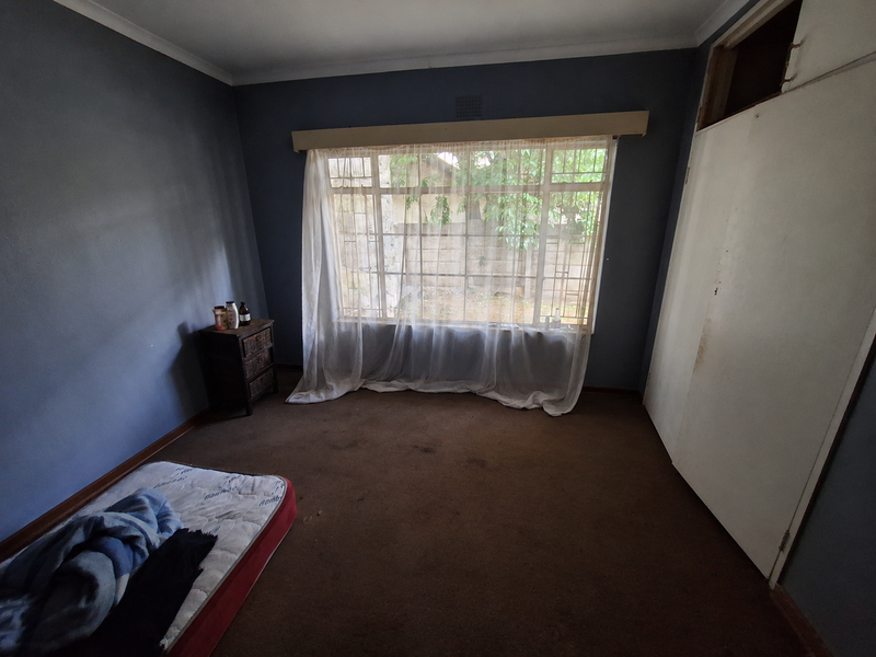 A bedroom featuring a large window, built-in wardrobe with missing panel, and carpet flooring. The room requires cosmetic updates to improve its overall condition.