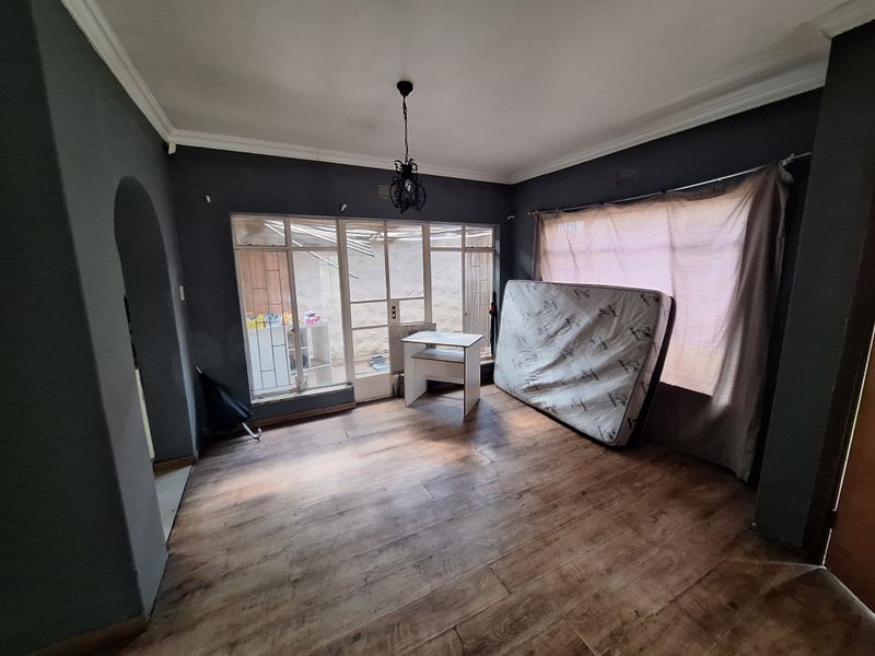 A spacious living room featuring laminate flooring, coved ceilings, and large aluminium-framed windows, offering a blank canvas for interior design updates.