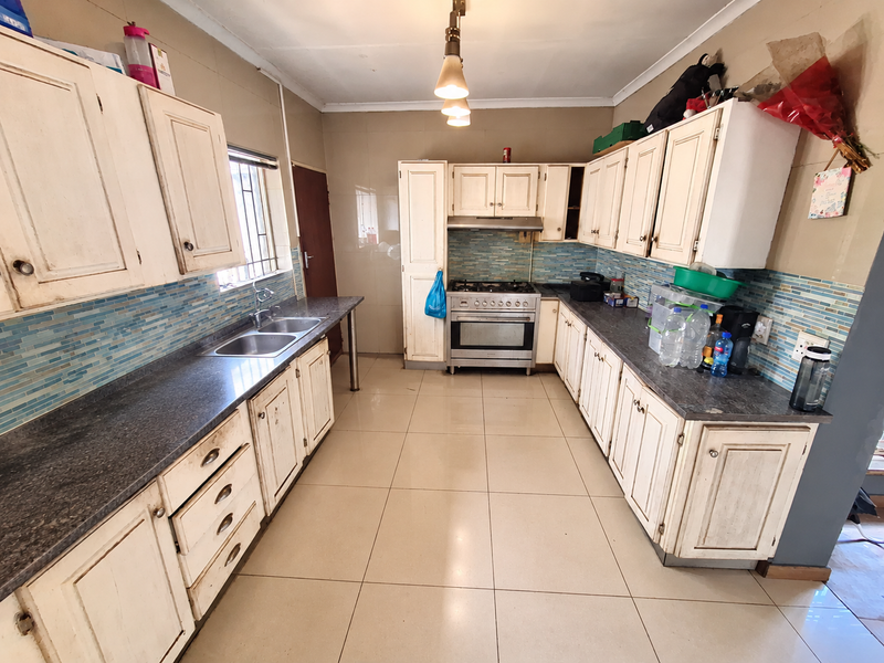A functional kitchen featuring built-in cabinetry, a gas stove with extractor fan, double basin sink, and tiled splashback with neutral floor tiles.