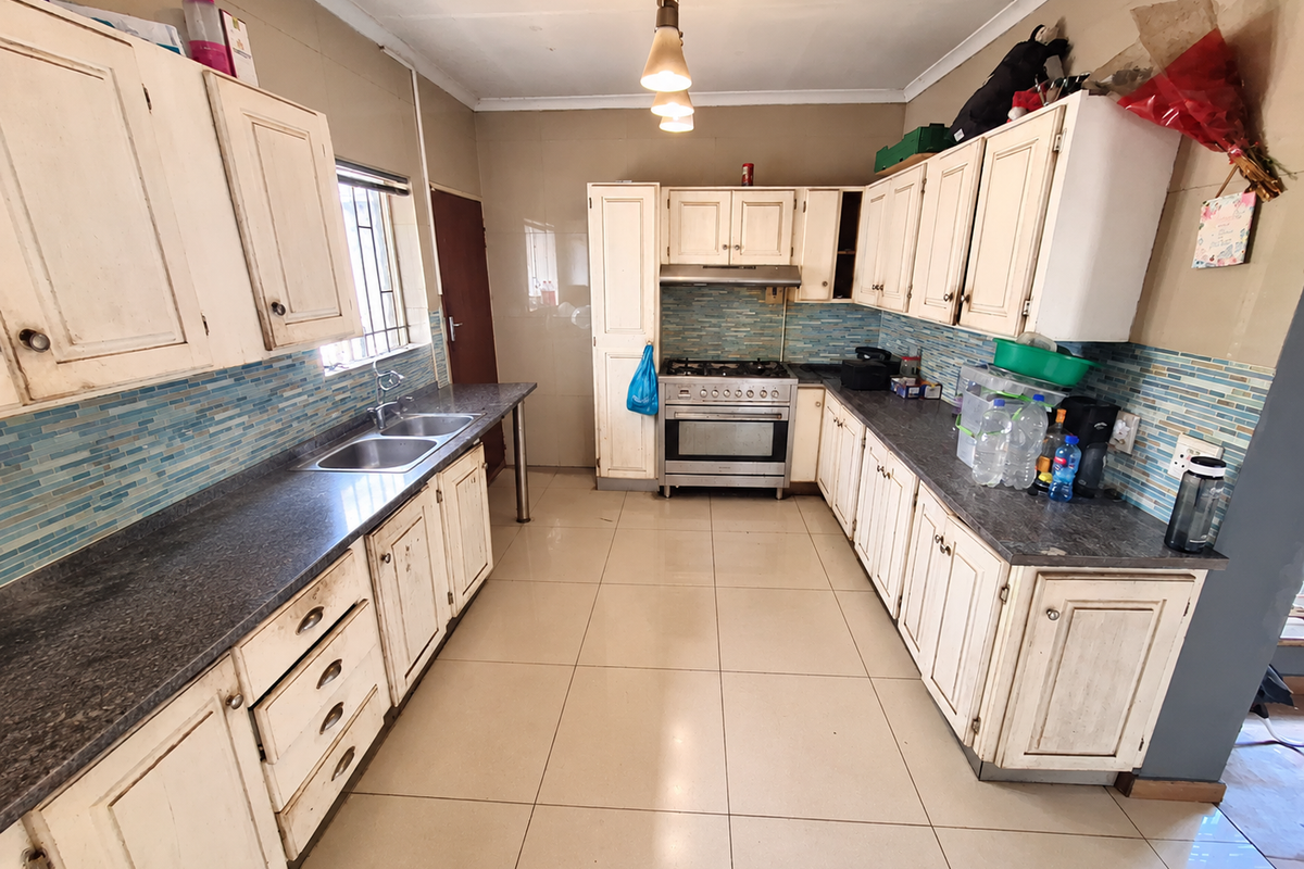 A functional kitchen featuring built-in cabinetry, a gas stove with extractor fan, double basin sink, and tiled splashback with neutral floor tiles.