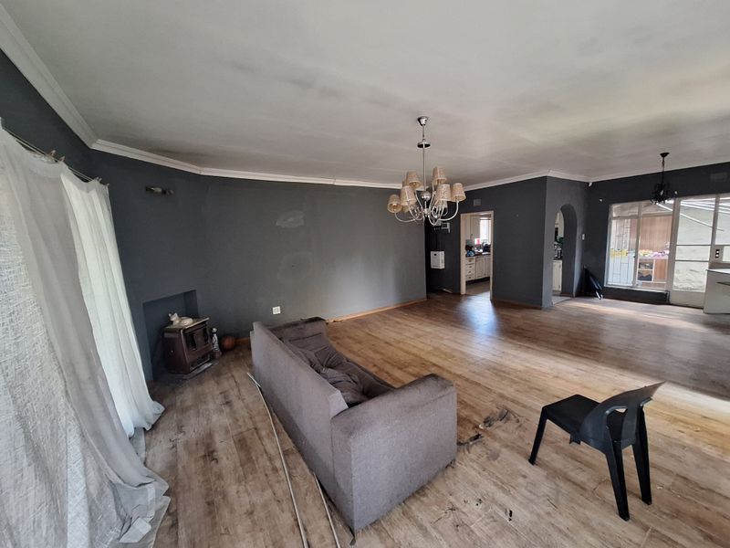 Spacious living area featuring hardwood flooring, a built-in wood burning fireplace, and an open-plan layout leading to the kitchen area.