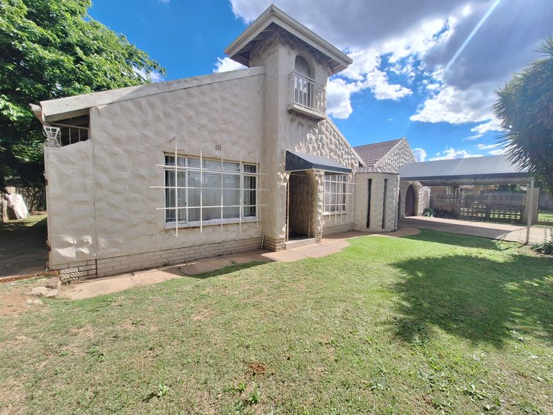 Front view of a house featuring textured stone-cladding, a balcony, and an attached carport with a paved driveway and lawn area.