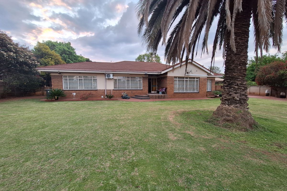 A spacious rear garden view of a single-story brick house featuring a tiled roof, security bars on windows, and an installed air conditioning unit.