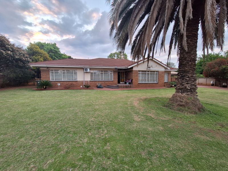 A spacious rear garden view of a single-story brick house featuring a tiled roof, security bars on windows, and an installed air conditioning unit.