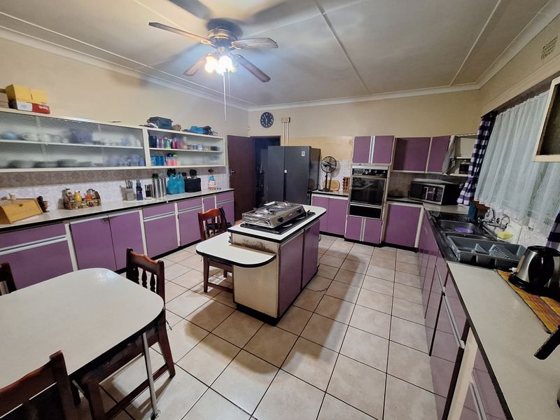 Spacious kitchen featuring extensive built-in cabinetry, a central island with cooktop, built-in oven, and tiled flooring, offering significant potential for modern renovation.