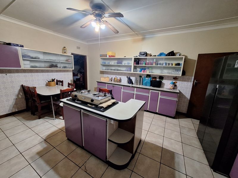 A dated kitchen featuring purple cabinetry, a central island with a cooktop, tiled flooring, and a tiled backsplash.