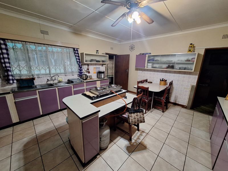Spacious kitchen featuring a central island with gas hob, ample built-in cabinetry, double sink, and tiled flooring, offering significant potential for modern renovation.