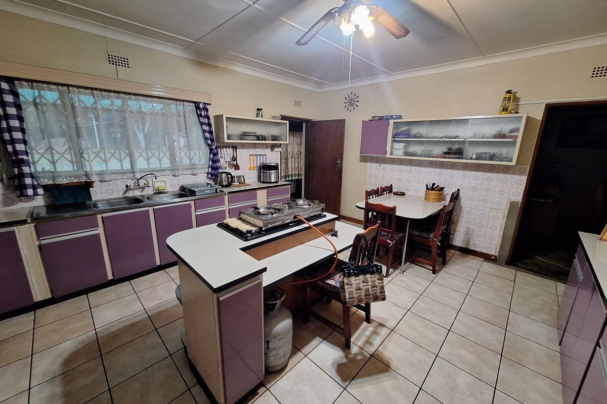 Spacious kitchen featuring a central island with gas hob, ample built-in cabinetry, double sink, and tiled flooring, offering significant potential for modern renovation.