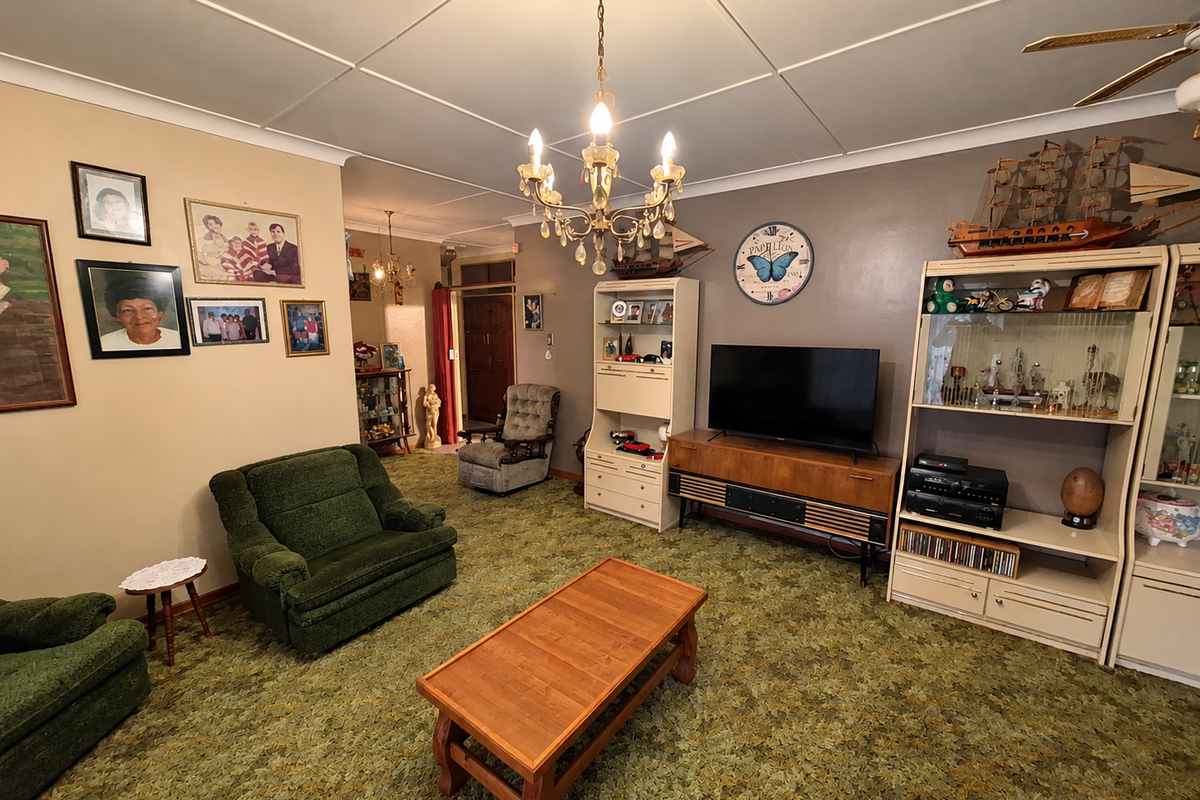 A spacious living room featuring a traditional chandelier, ceiling fan, and coved ceilings, offering a dated interior ready for modern updates.