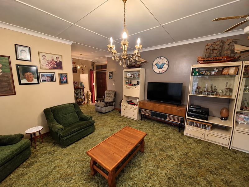 A spacious living room featuring a traditional chandelier, ceiling fan, and coved ceilings, offering a dated interior ready for modern updates.
